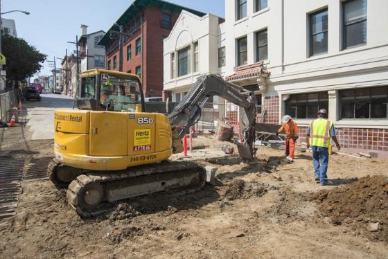 Construction excavation at Stockton and Washington streets with yellow excavator and workers in safety vests.