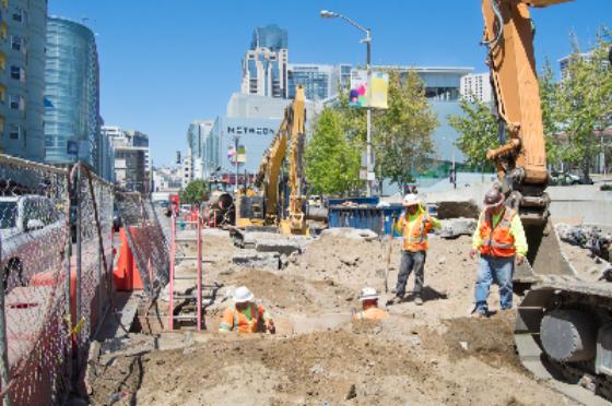 Construction site with heavy equipment and workers at future Yerba Buena Moscone Station in urban area.