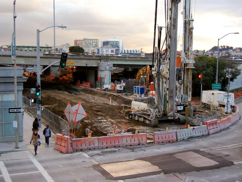 Construction site with tunnel launch box equipment, barriers, and excavation work on 4th Street near bridge underpass.
