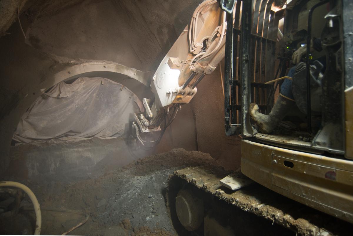 Excavator with grinding wheel breaking out concrete bulkhead inside north platform cavern side drift.