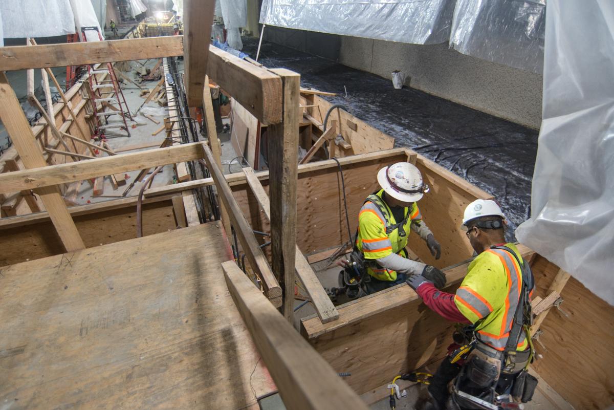 Two workers in safety gear construct wooden concrete forms and install rebar inside a station box excavation.