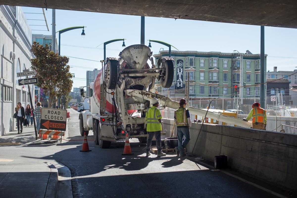 Concrete mixer truck delivers material to construction site at 4th and Brannan station under highway overpass.