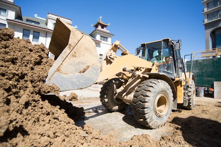 Wheel loader with bucket removing excavated soil from construction site near residential buildings.
