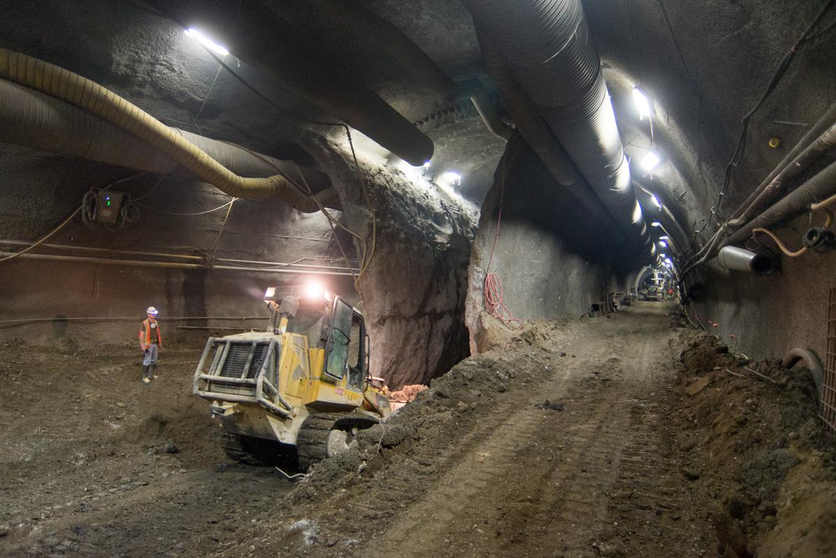 Bulldozer excavating soil in underground tunnel with workers and LED lighting during transit station construction.