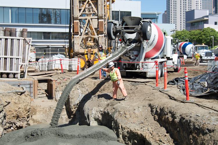 Worker directs concrete pump from mixer truck during 4th Street construction project.