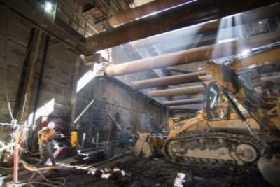 Construction crew operating excavator and jackhammer equipment in underground shaft at night.