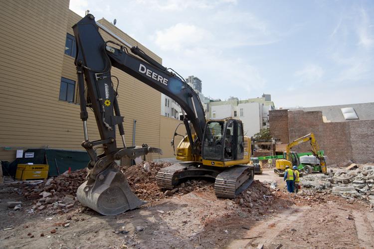 Deere excavator demolishing Pagoda Palace building on Stockton Street with construction crew and equipment nearby.