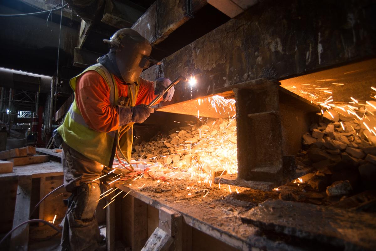 Worker in safety vest cutting steel bracing inside Chinatown Station headhouse during repairs.