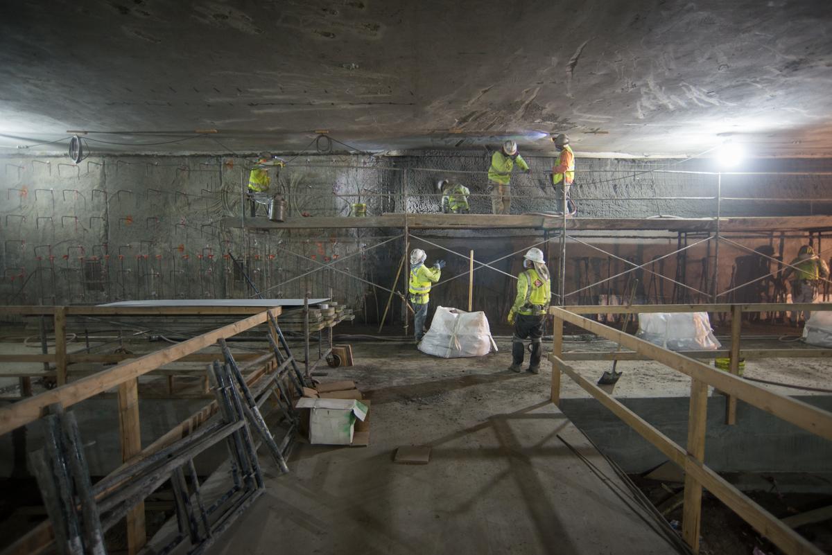Workers in safety vests clean concrete walls inside underground transit station construction site.