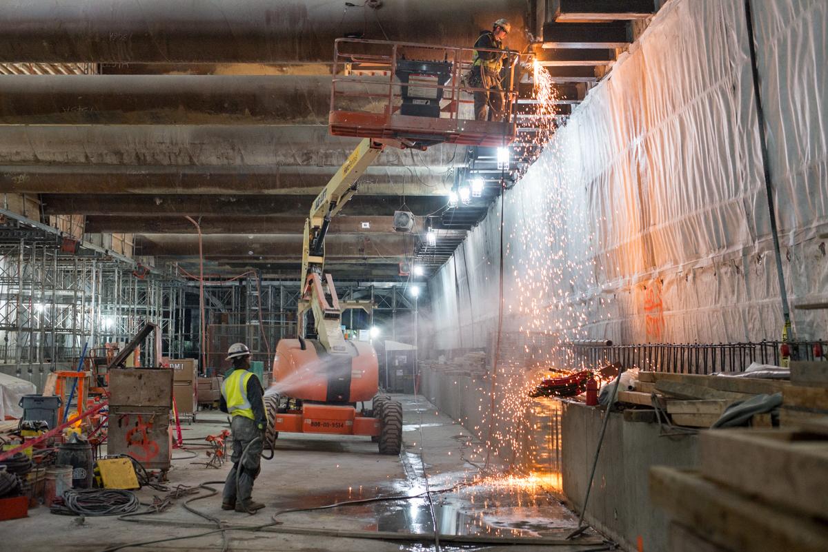 Worker welding steel brackets inside Union Square/Market Street station construction site.