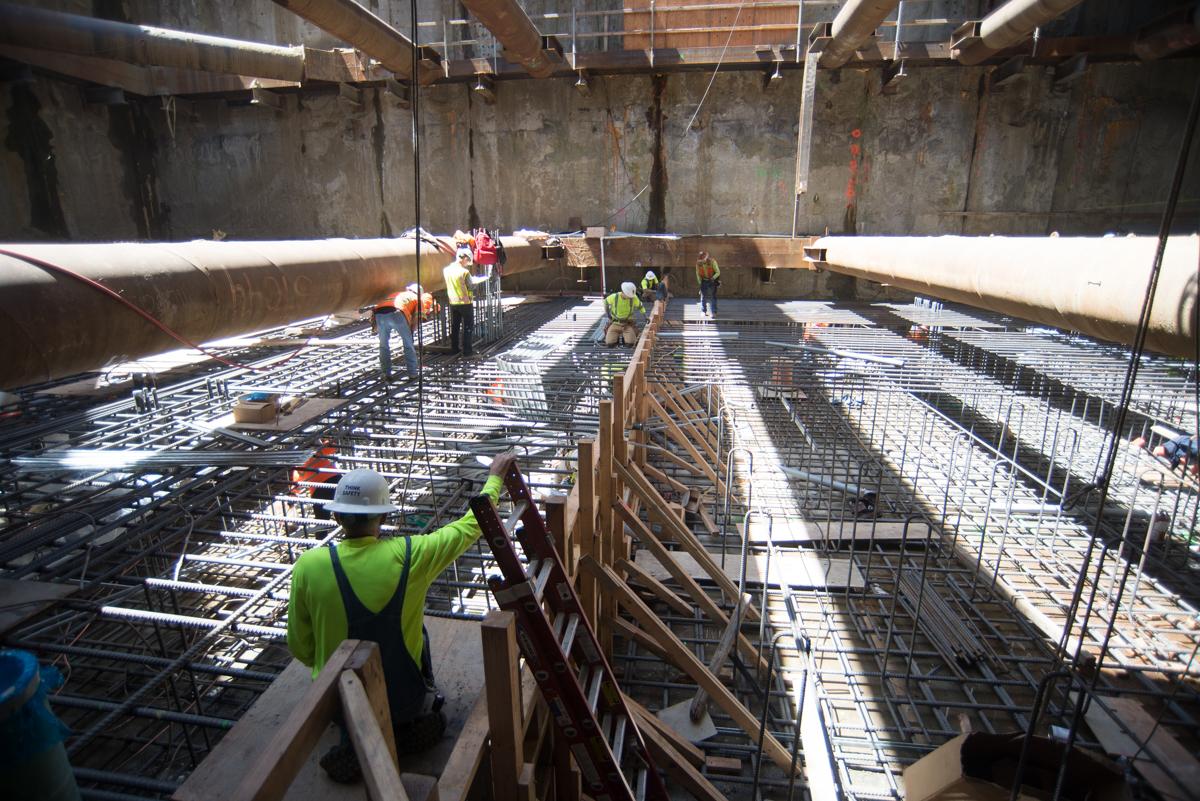 Construction workers in safety vests install steel rebar reinforcement in underground transit station foundation.