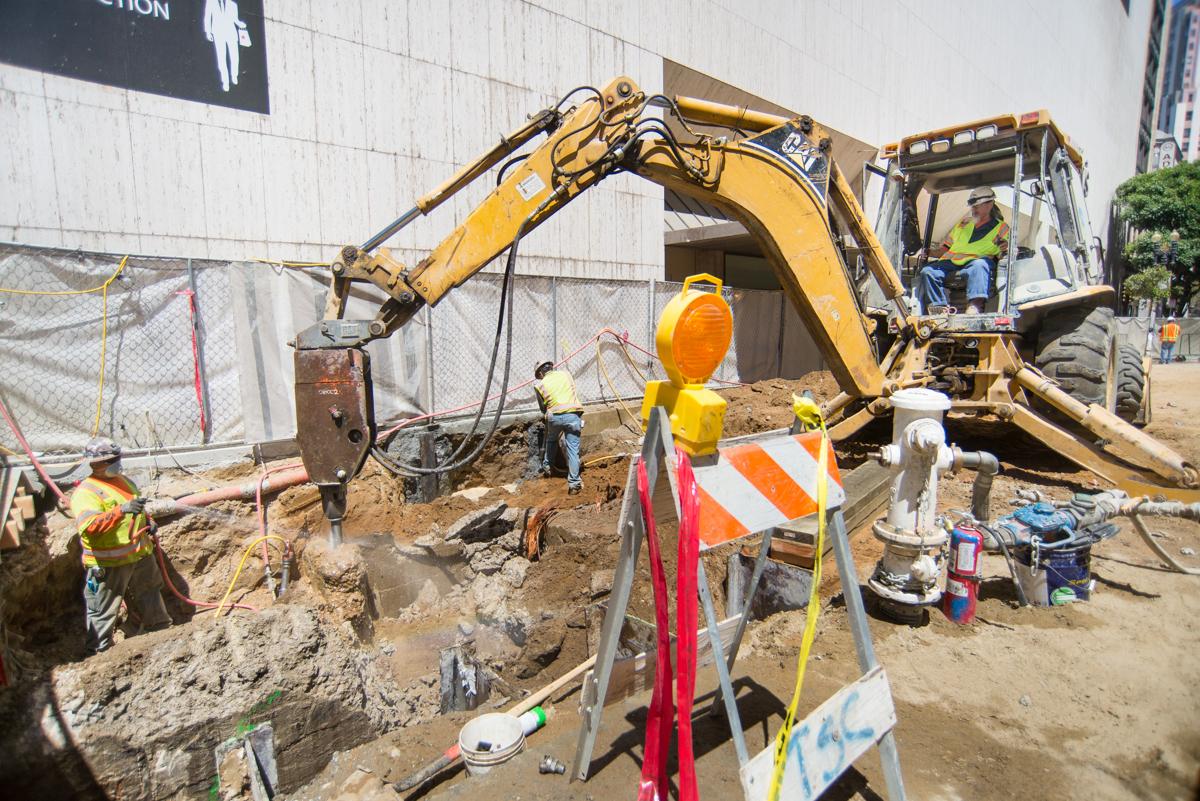 Construction excavation at Stockton Street station with yellow excavator and workers in safety gear.