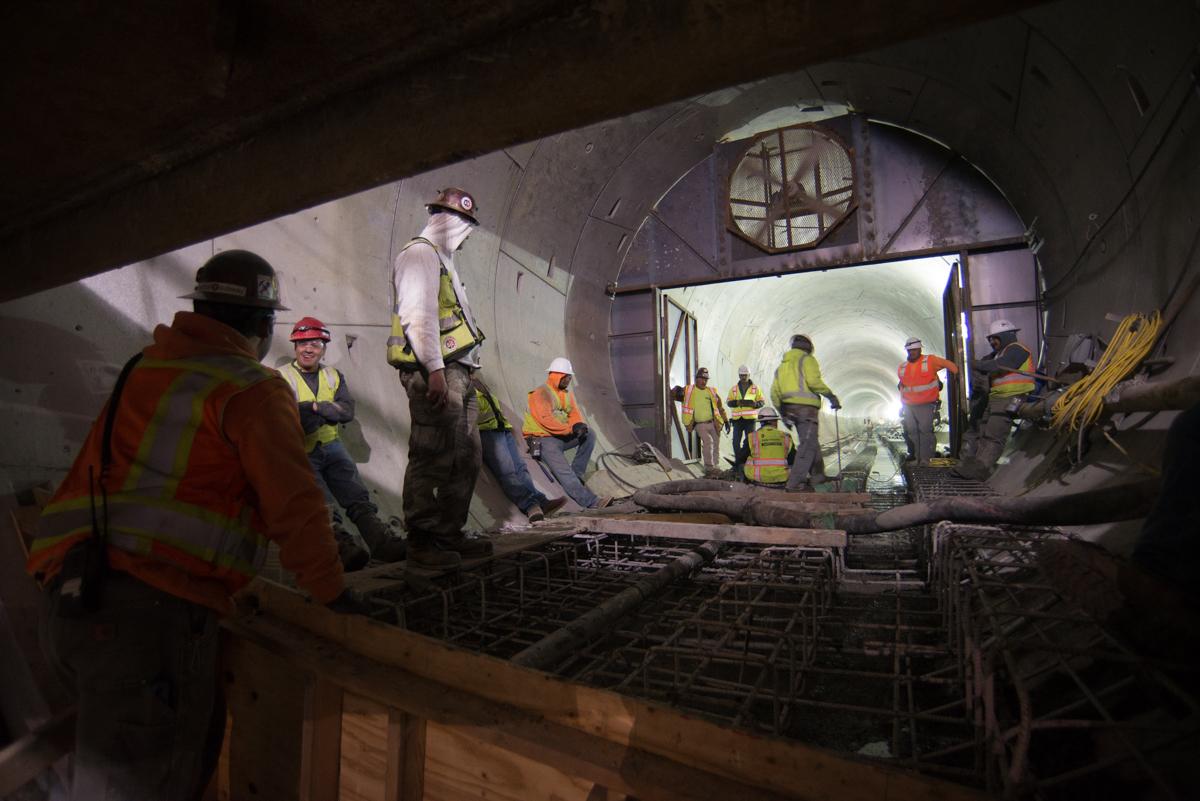 Construction workers in safety gear install rebar and prepare concrete pour inside tunnel under construction.