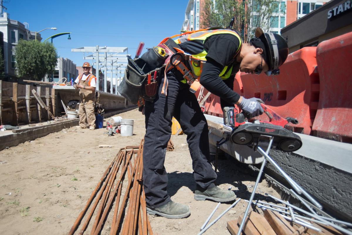 Worker in safety gear cutting steel rods at 4th and Brannan Station construction site.