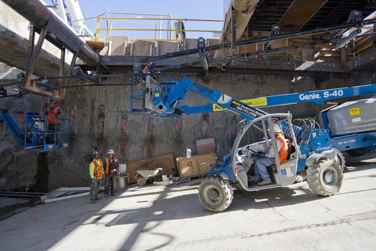 Genie S-40 lift platform at tunnel launch site with workers and conveyor system for transporting tunnel excavation materials.