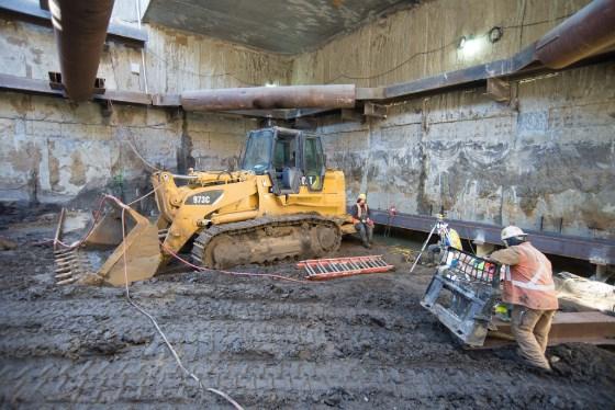 Yellow bulldozer and workers performing excavation work at underground transit station construction site.