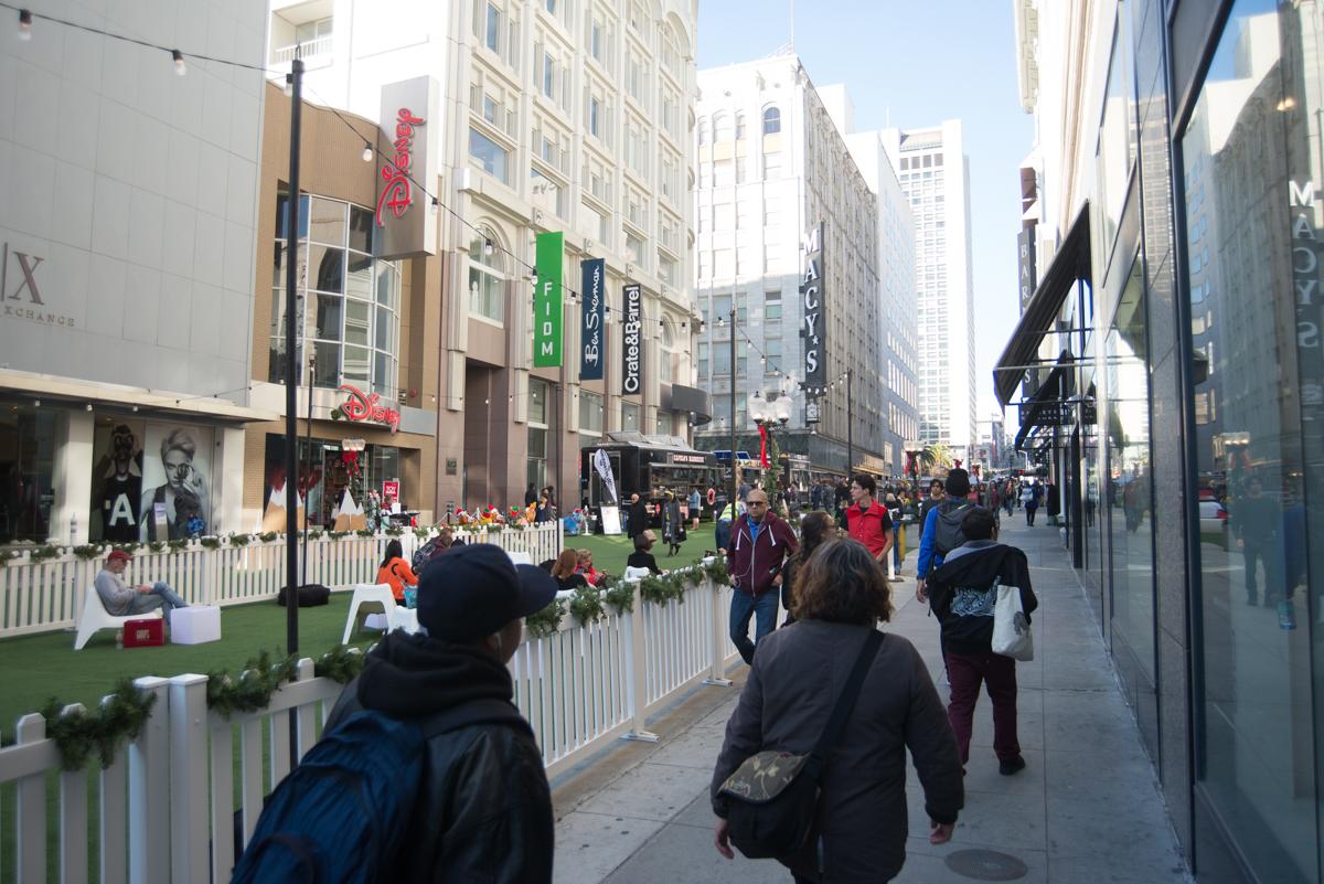 Crowded pedestrian street decorated with white fencing and greenery during holiday shopping season in downtown San Francisco.