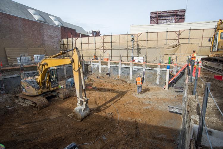 Construction site with excavator, concrete foundation posts, and workers in safety gear at tunnel boring machine shaft.