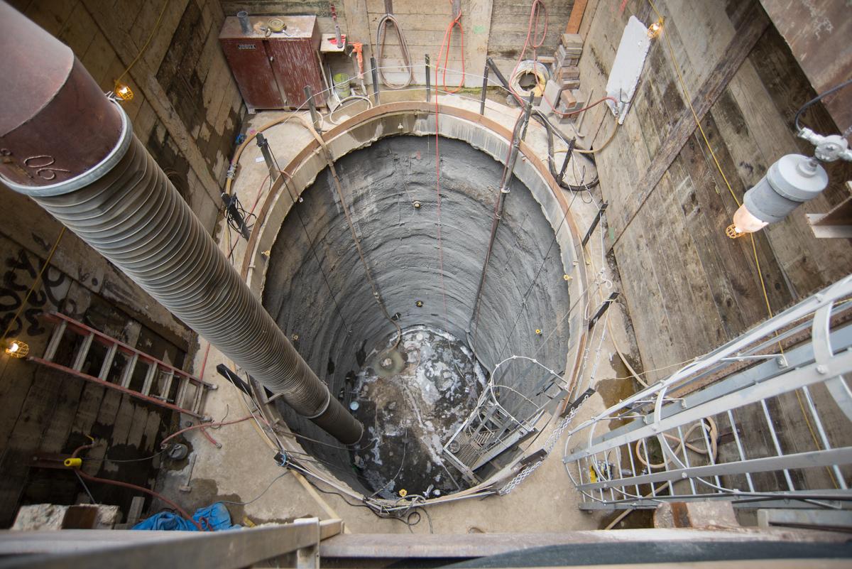 Overhead view of underground tunnel excavation shaft with concrete walls, metal scaffolding, and construction equipment.