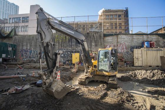 Excavator and construction equipment at Chinatown Station construction site with completed station walls.