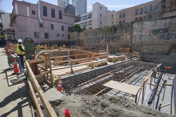 Construction site with wooden framing and steel rebar for future Chinatown Station, surrounded by urban buildings.