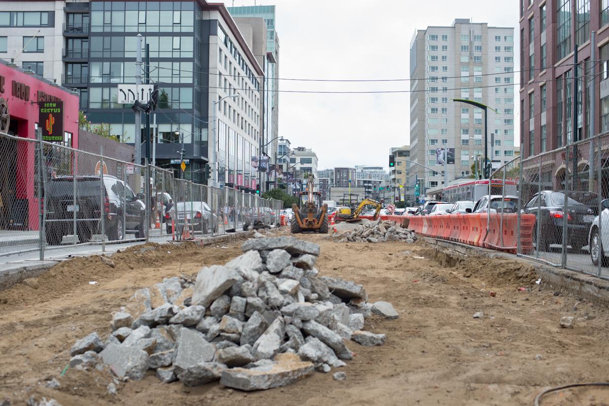 Construction site on 4th Street with debris pile, heavy equipment, and surrounding urban buildings.