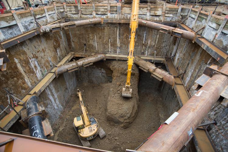 Excavation pit with two yellow excavators and wooden shoring walls during tunnel boring machine retrieval construction.