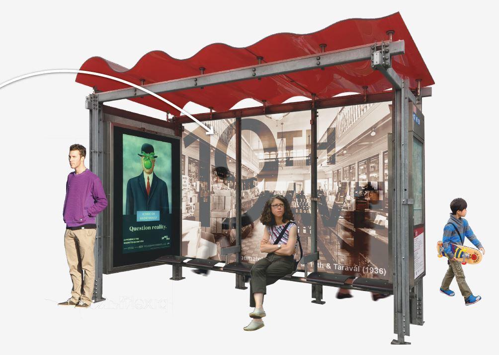 Modern transit shelter with red canopy, digital display, and glass panels, occupied by waiting passengers in urban setting.