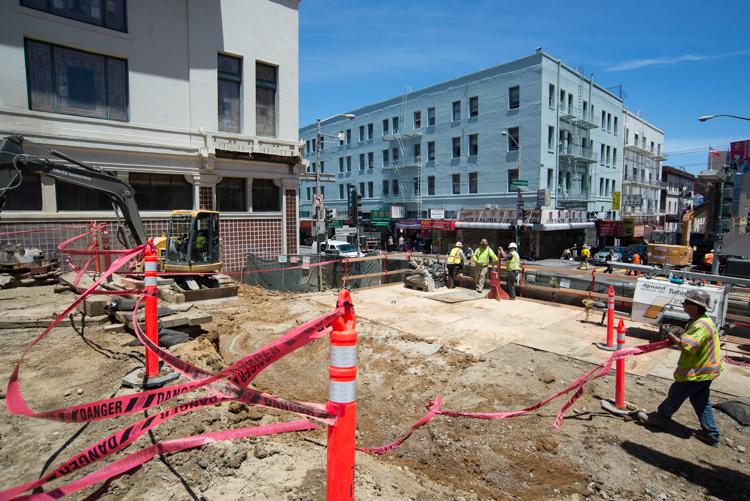 Construction site at Stockton and Washington with safety barriers, equipment, and workers in high-visibility gear.