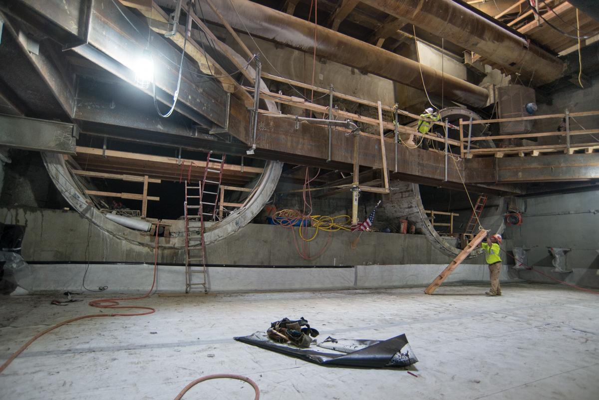 Construction workers install base slab and waterproofing inside underground transit station box.