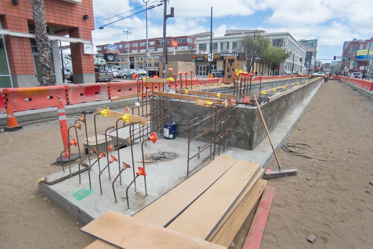 Construction site on 4th Street showing excavated foundation walls, steel reinforcement, and soil backfill between two trackways.