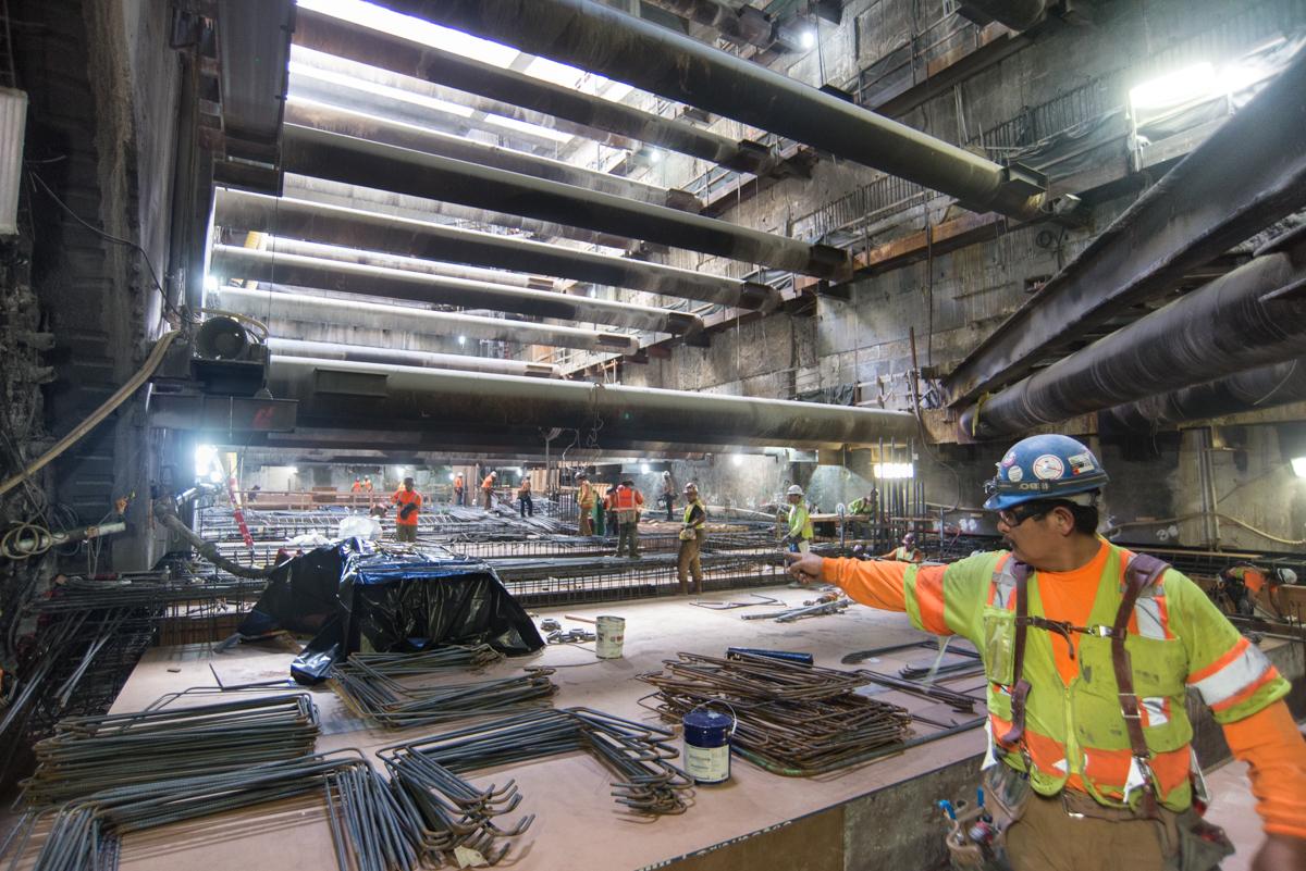 Construction workers in safety gear place rebar on concrete forms inside a subway tunnel under construction.