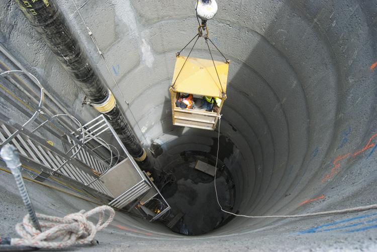 Workers in yellow safety box descending into deep underground shaft on Ellis Street.
