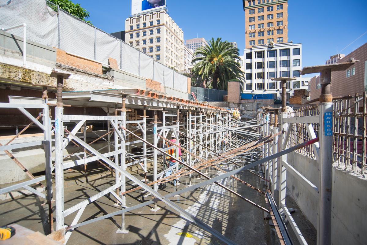 Union Square Garage ramp under construction with steel scaffolding and safety fencing, downtown buildings visible.