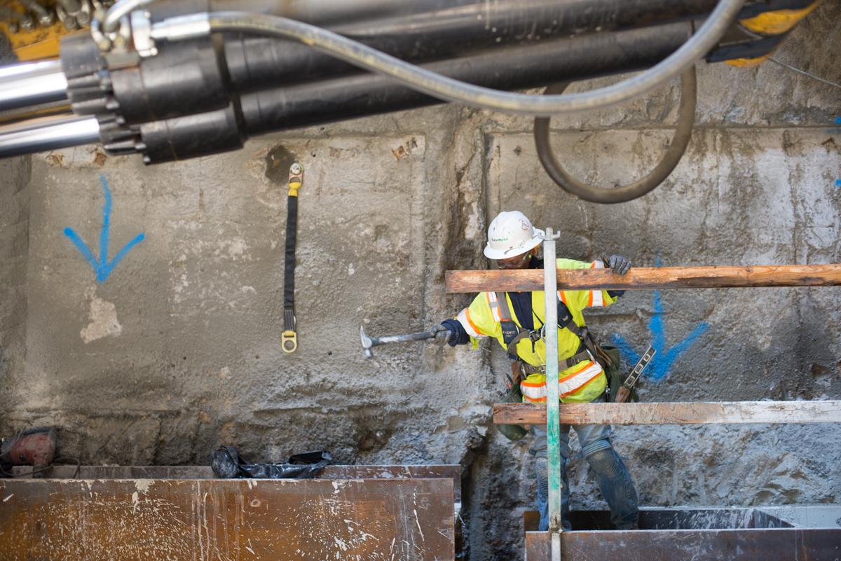 Worker in safety gear assembling railing on steel beams inside underground construction shaft.