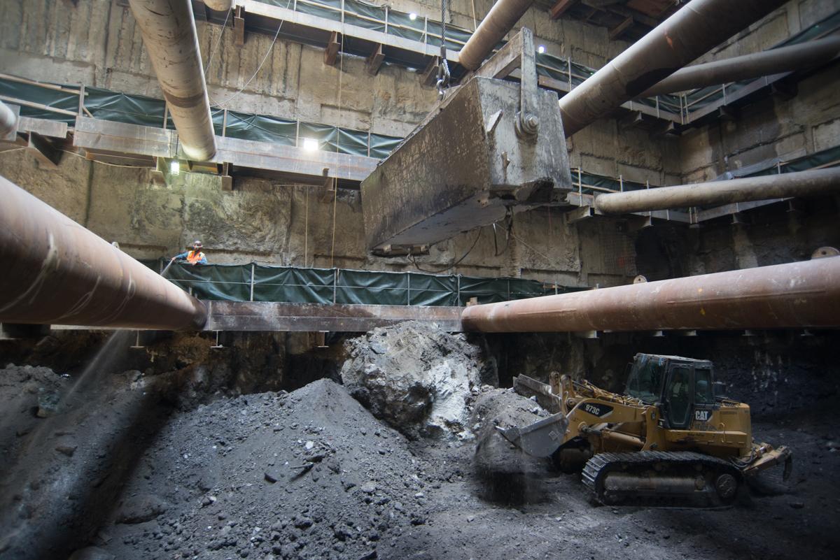 Underground construction site with excavator, concrete pipes, and debris beneath industrial infrastructure.
