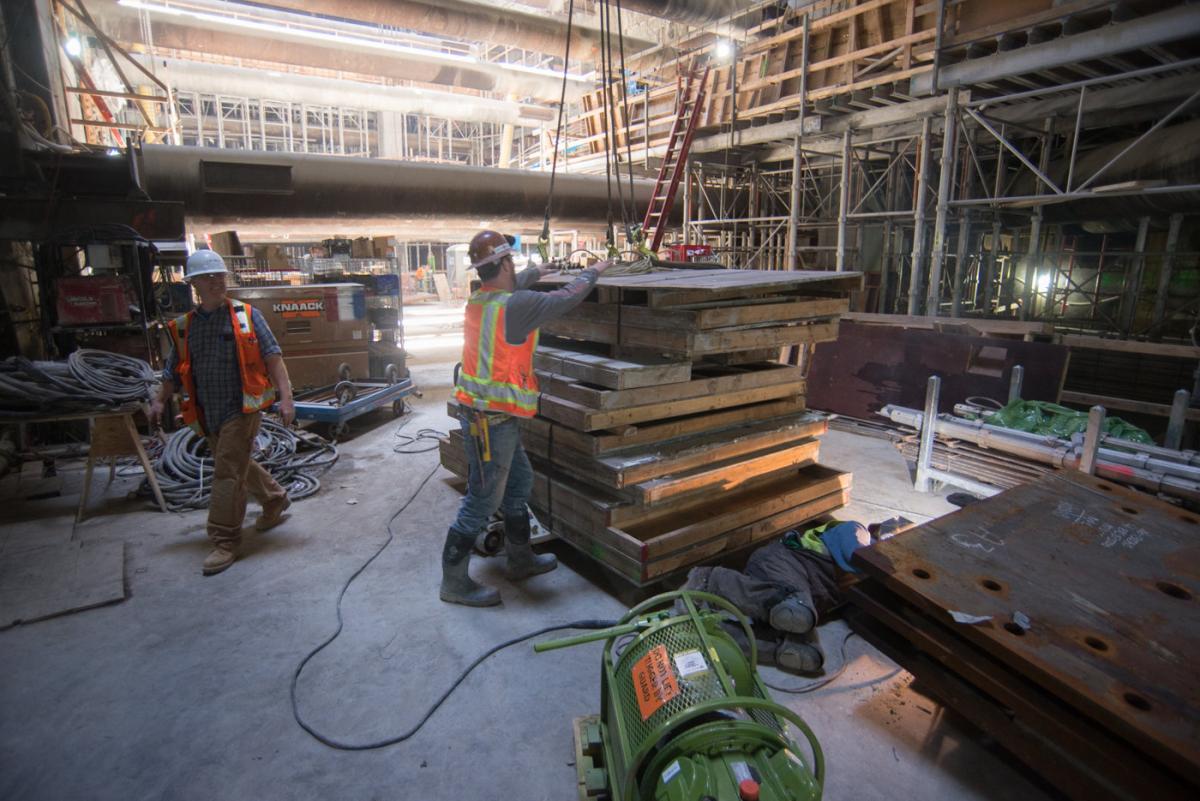 Workers in safety gear prepare steel plates and formwork sections for lifting inside a construction headhouse.