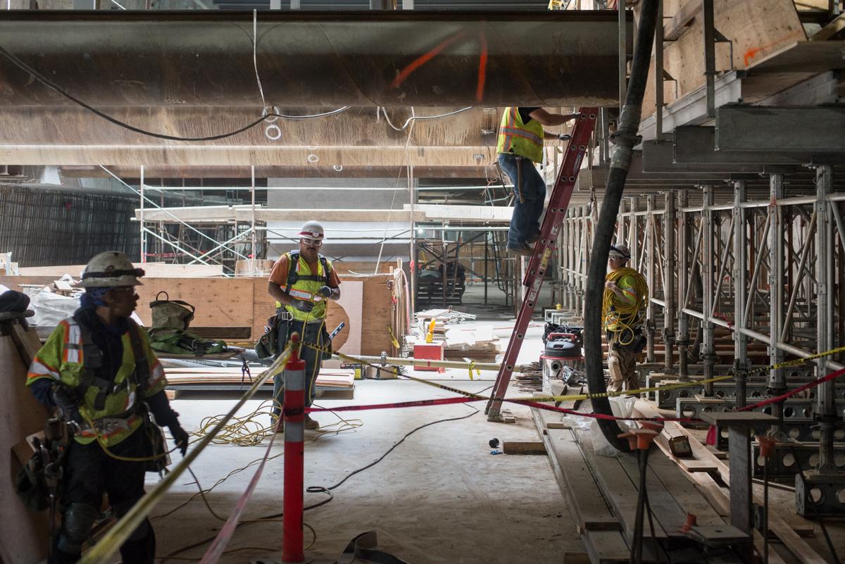Construction workers in safety vests work on formwork for concrete wale encasement beams inside a station box excavation.