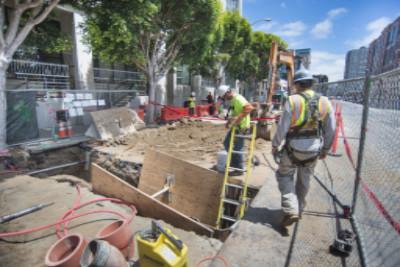 Construction workers in safety gear excavate and upgrade utilities at an urban transit work site.