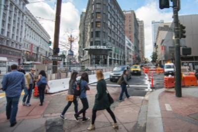 Pedestrians cross at Ellis and Stockton streets with traffic and construction barriers visible in downtown San Francisco.