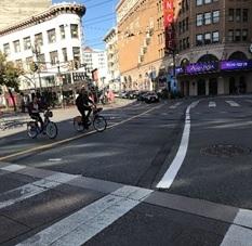 Cyclist riding on Market Street crosswalk with pedestrians and buildings visible.