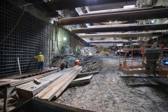 Underground construction site with workers assembling rebar cage for interior wall at Chinatown Station.