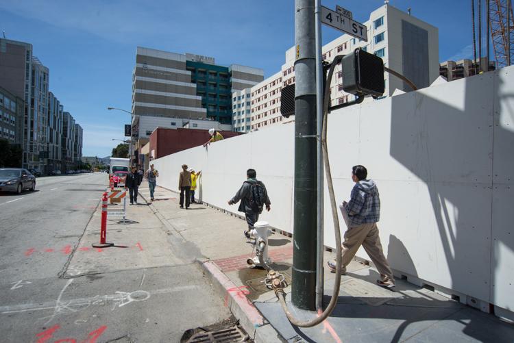 White temporary barrier installed on 4th Street sidewalk with pedestrians and construction workers nearby