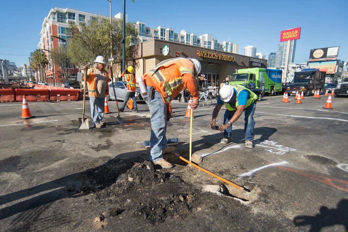 Construction workers repair a pothole at an urban intersection during a utility infrastructure project.