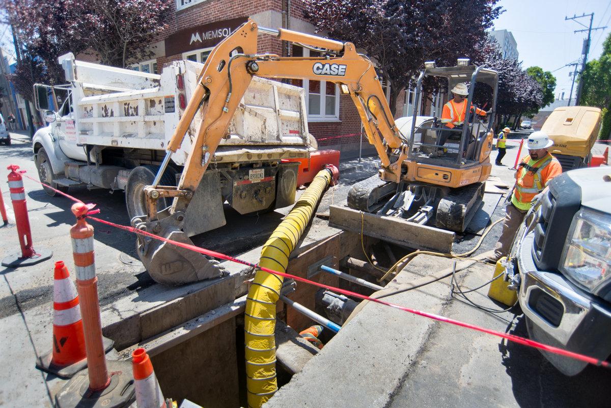Construction crew performs sewer tie-in work on 4th Street using excavator and utility equipment.