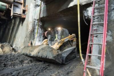 Excavator loading dump truck with excavated soil at underground station construction site.