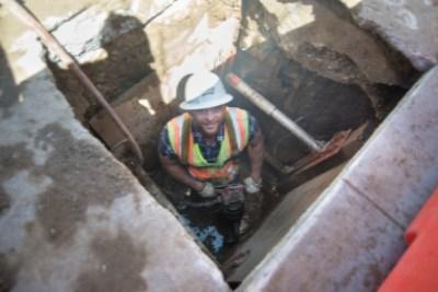 Worker in safety gear inside underground utility vault at street intersection.