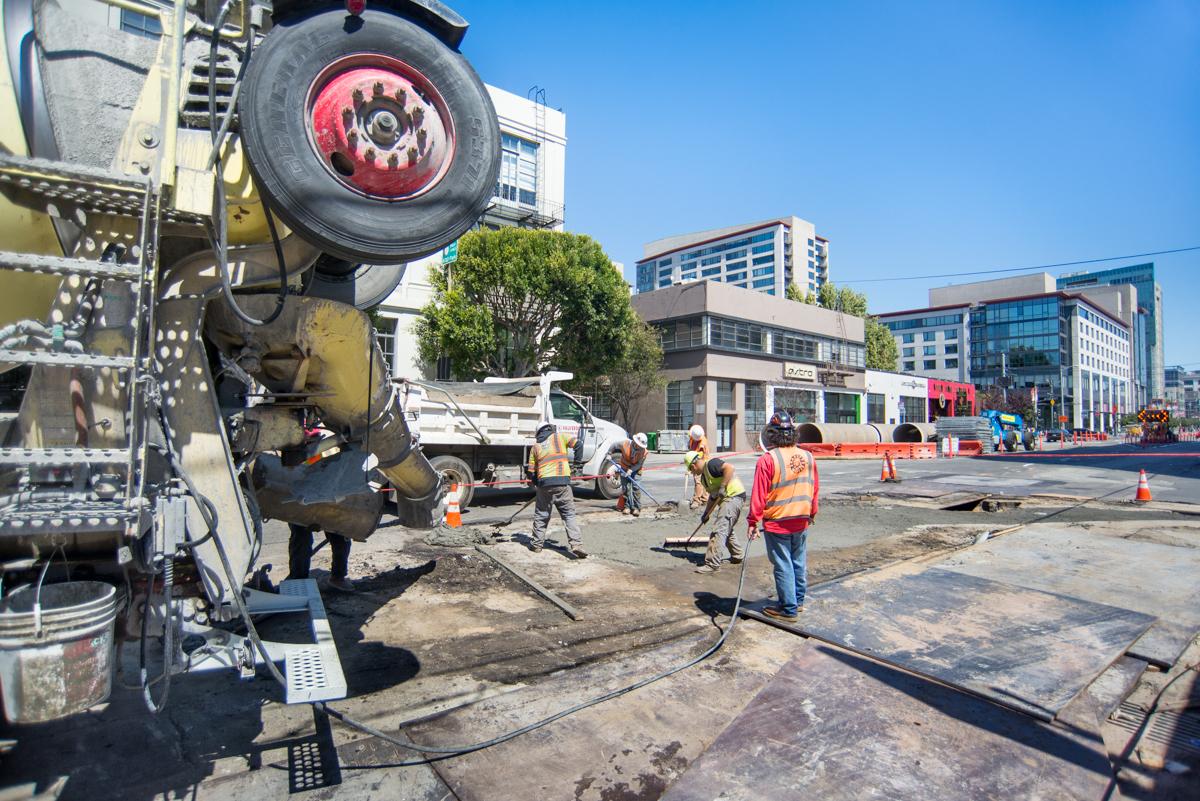 Concrete mixer truck and workers performing roadway restoration at an urban construction site.