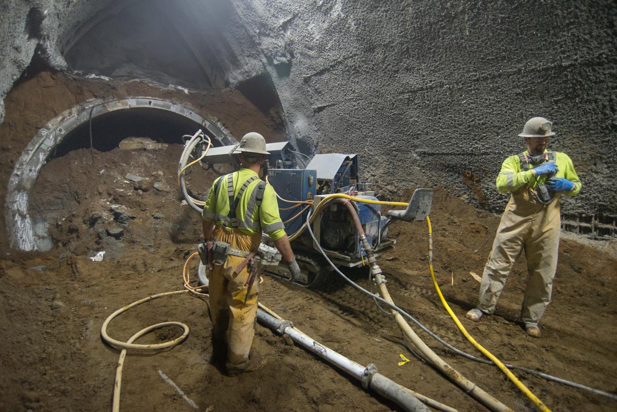 Workers operate shotcrete equipment during underground tunnel excavation for transit construction.
