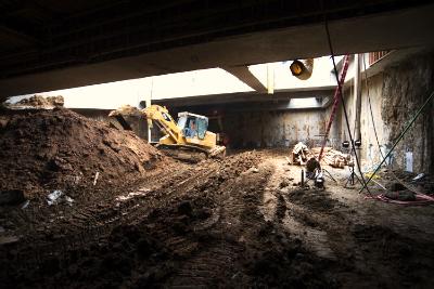 Underground construction site beneath bridge with excavator and workers removing soil
